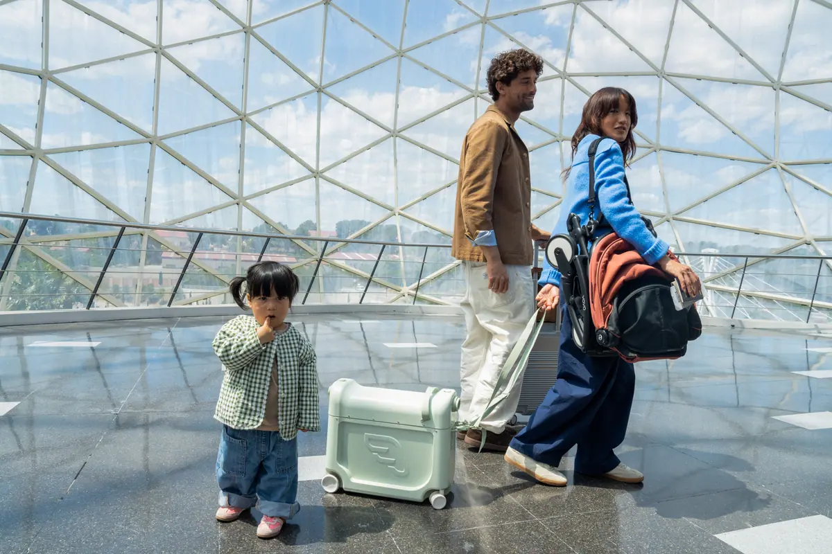 ครอบครัวในสนามบิน คุณพ่อสะพายรถเข็น YOYO5 ที่พับแล้ว ลูกยืนข้างกระเป๋า JetKids BedBox