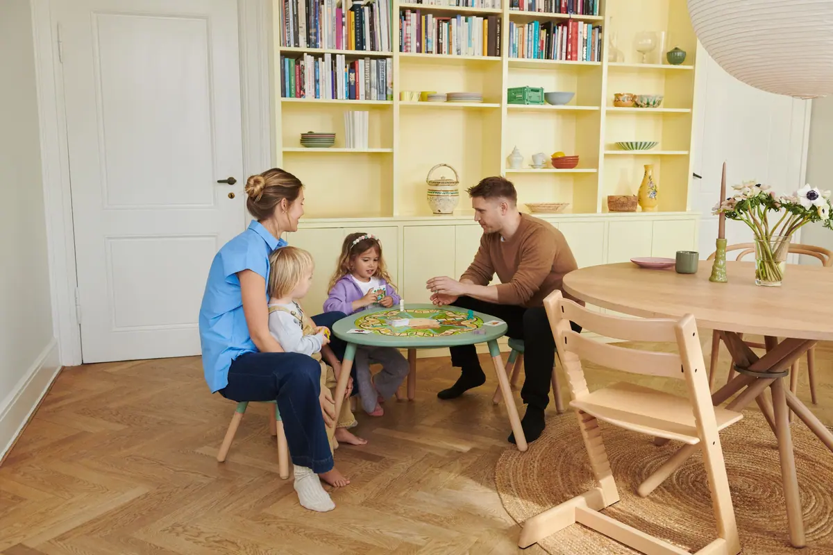 ครอบครัวสี่คนนั่งเล่นบอร์ดเกมรอบโต๊ะ Stokke MuTable สีเขียวในห้องนั่งเล่น