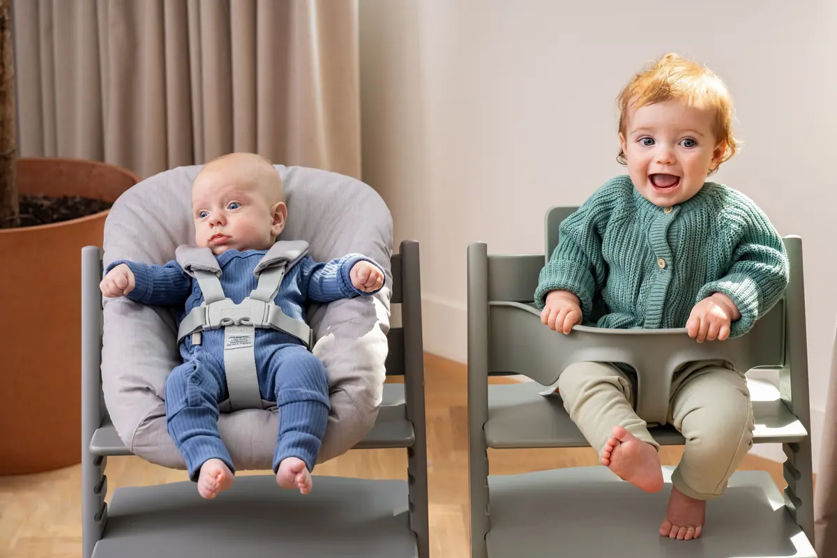 เก้าอี้ Tripp Trapp สองตัว ตัวหนึ่งมีเด็กแรกเกิดใน Newborn Set อีกตัวมีเด็กเล็กหัวเราะใน Baby Set