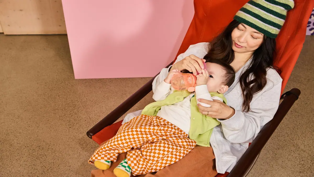 แม่นั่งเก้าอี้ผ้าใบป้อนนมจากขวด Tommee Tippee ให้ลูกเล็ก