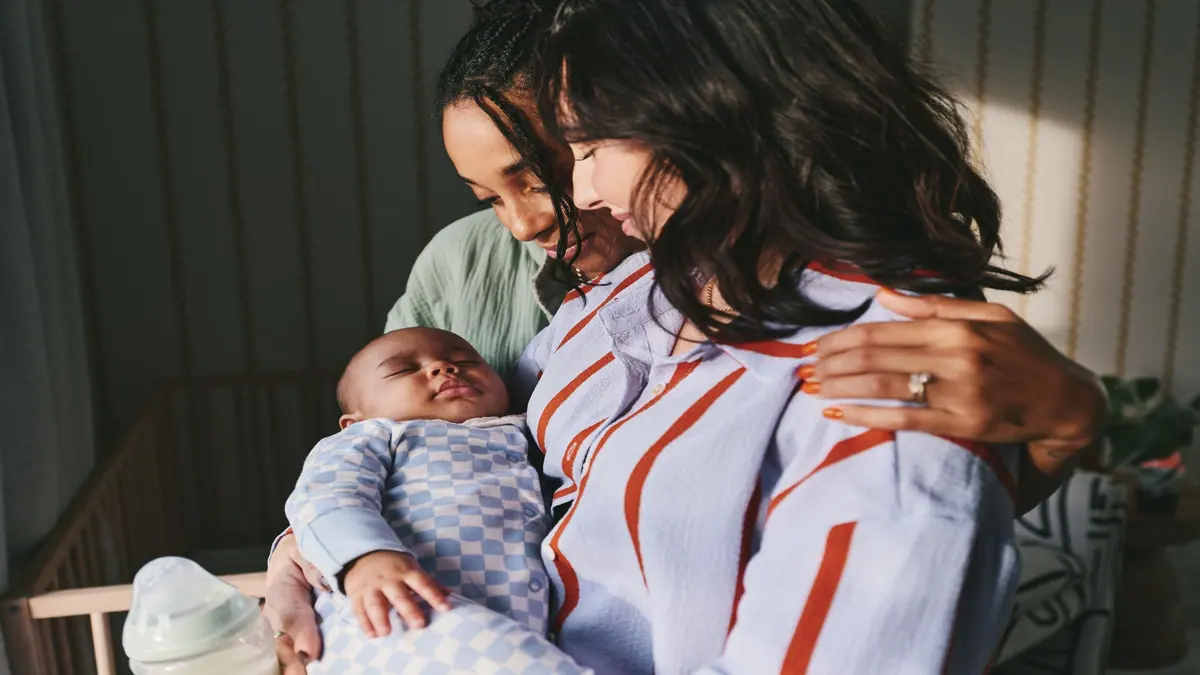 พ่อแม่กอดลูกน้อยที่หลับอยู่ มีขวดนม Tommee Tippee วางข้างๆ