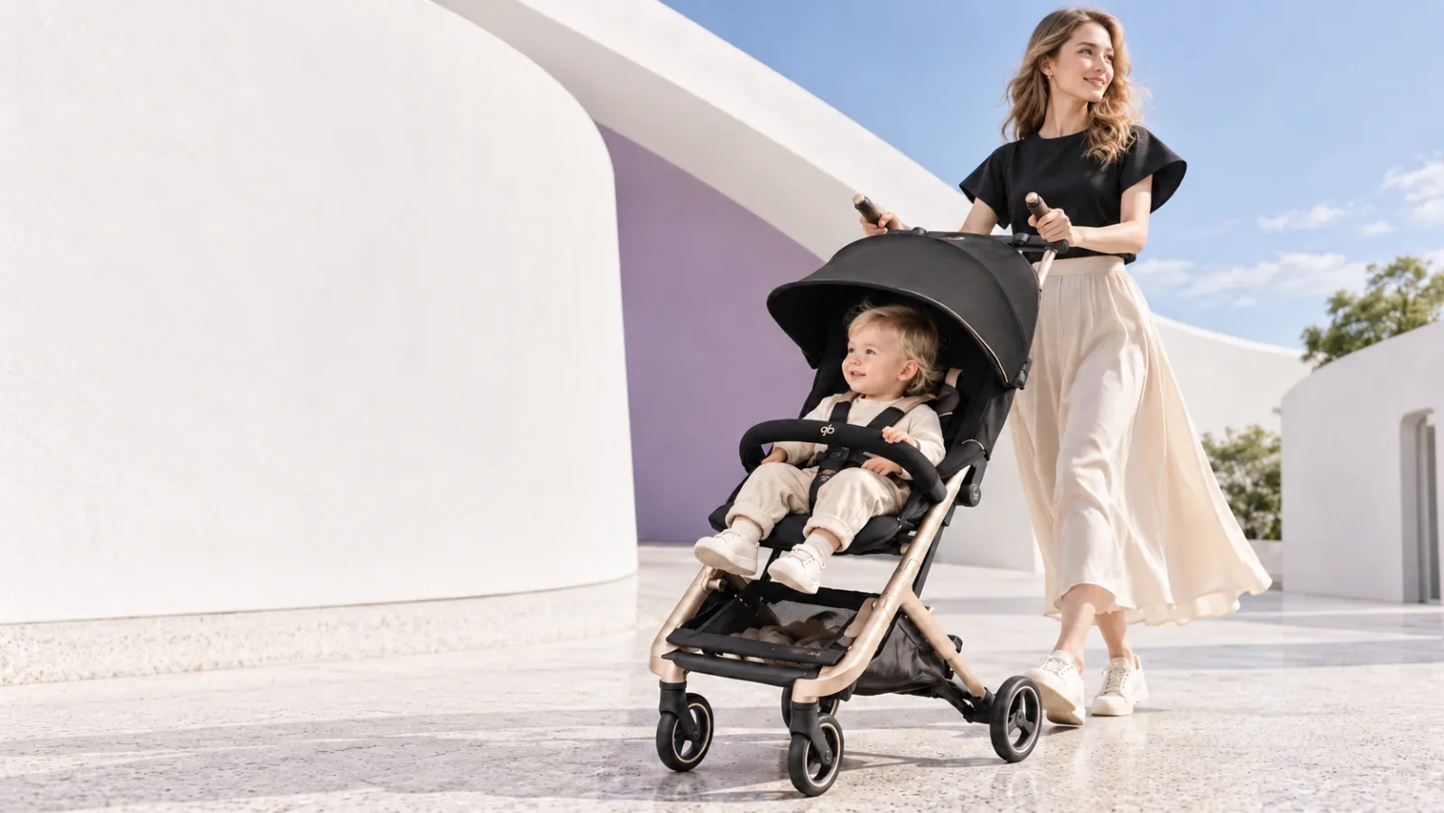 子どもを乗せた GB Pockit GO コンパクトベビーカーを押して白い建物の前を歩くお母さん