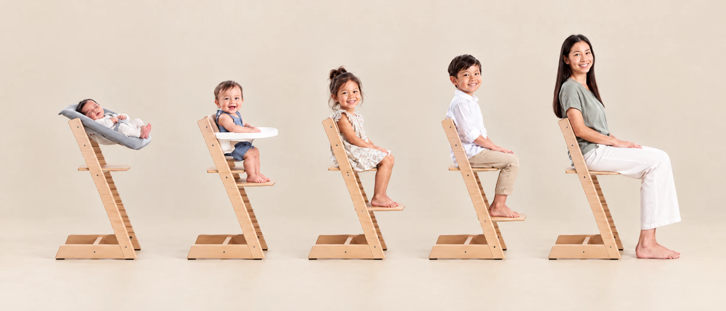 並んだ5脚の Stokke Tripp Trapp：Newborn Set の新生児、トレイ付き Baby Set の幼児、大きい子ども、そしてお母さん